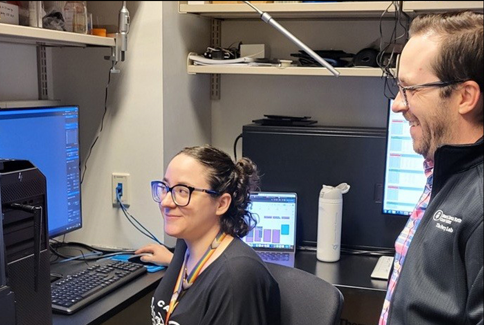 a woman sitting in front of a computer with a man looking over her shoulder