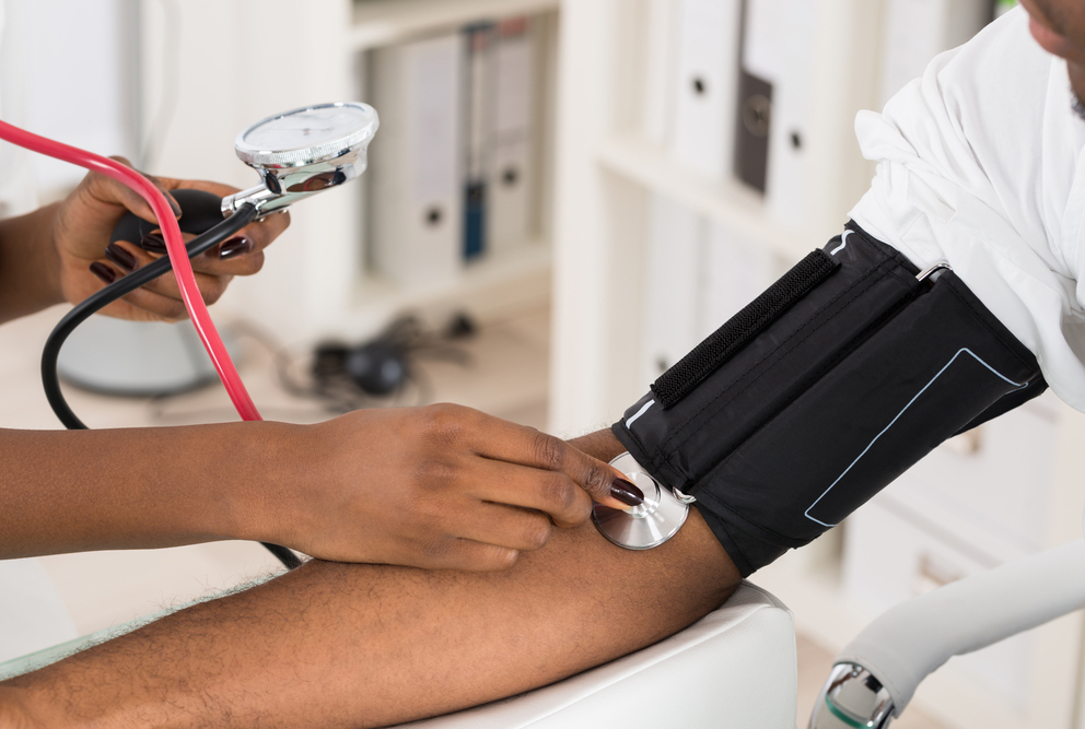 Photo of a hand holding a stethoscope on a man&#039;s arm with a blood pressure cuff