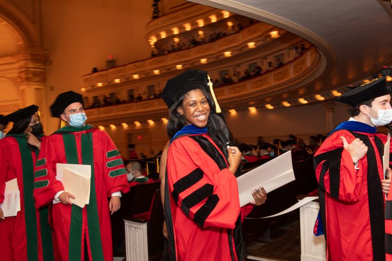 a young woman smiling as she walks down the aisle at graduation